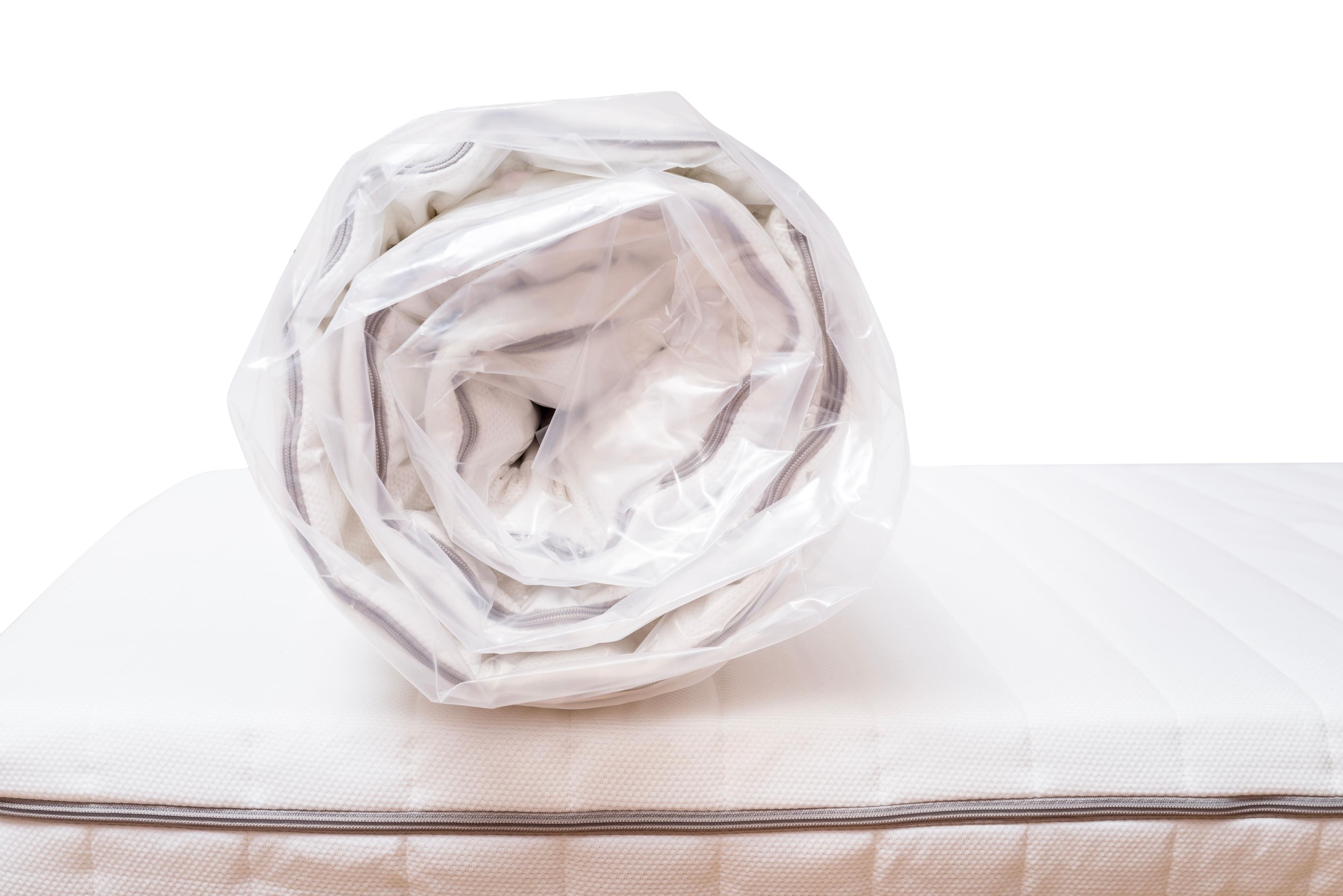 Aufgerollte Matratze in transparenter Plastikfolie auf einer weiteren Matratze liegend.